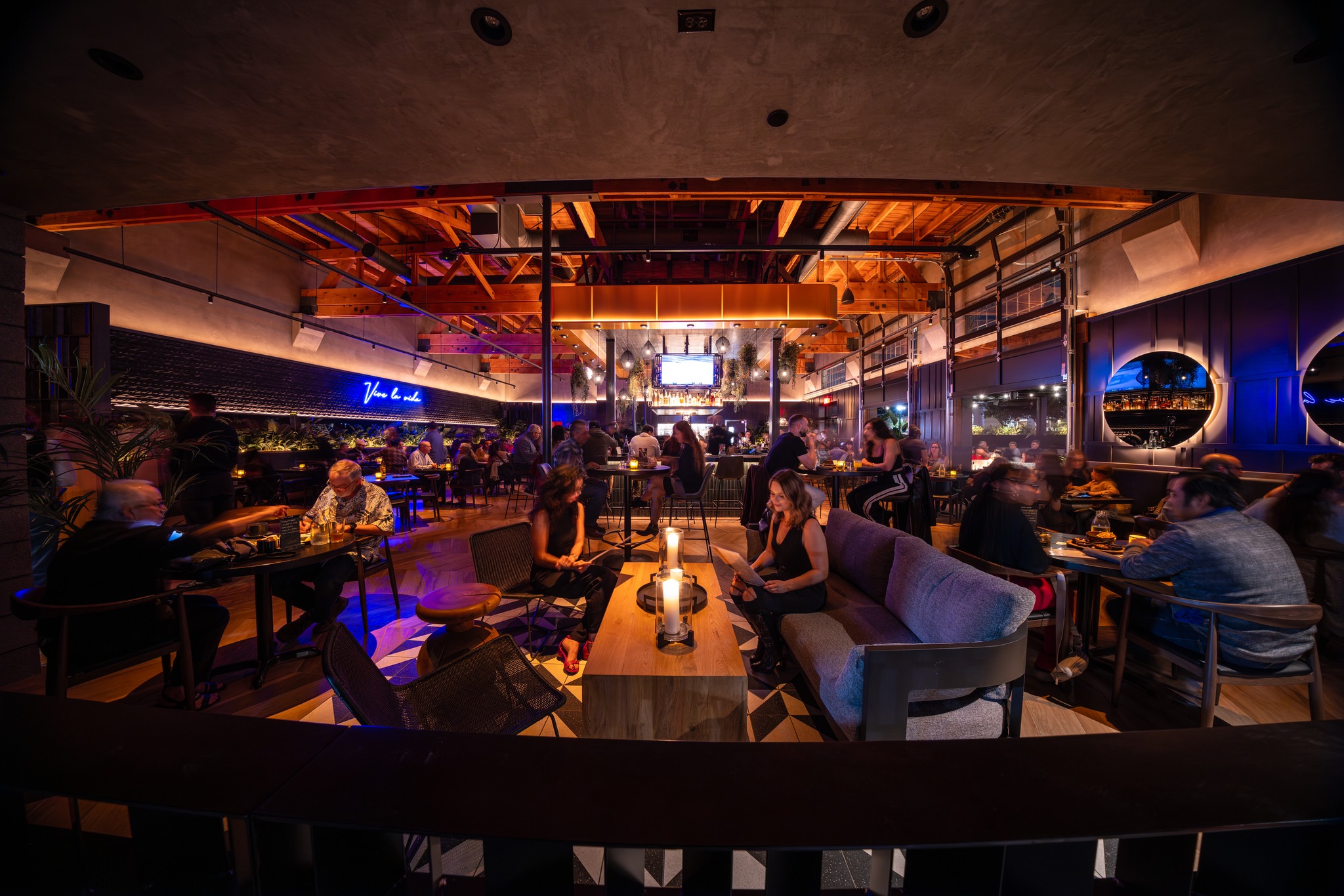 Spacious, modern restaurant interior with exposed beams and many patrons.