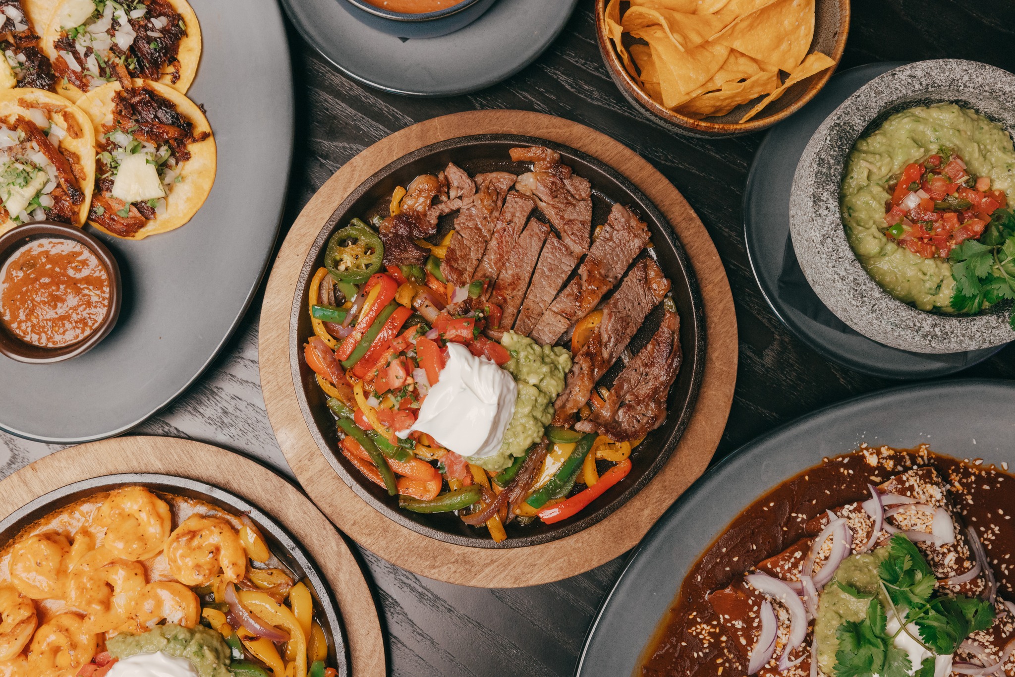 Multiple Mexican dishes: steak fajitas, tacos, guacamole, shrimp, and enchiladas.