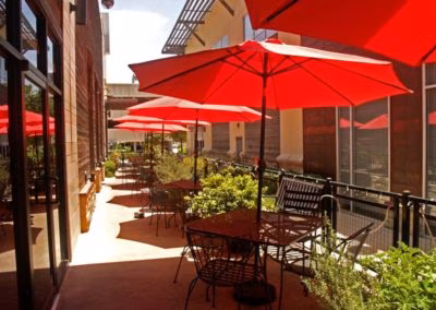 Outdoor restaurant patio with red market umbrellas and tables.
