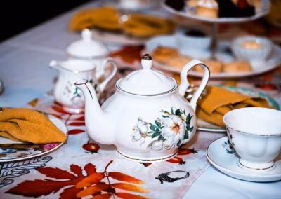 White floral teapot, teacup, and saucer on an autumn leaf tablecloth.