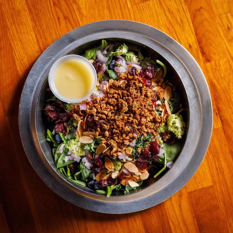 Salad with greens, almonds, berries, brown crumble, and dressing cup.