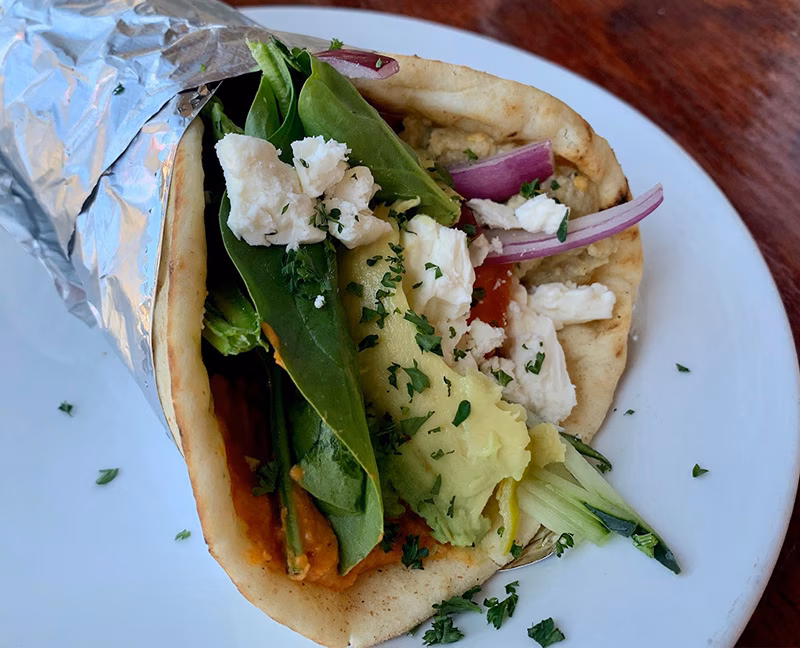 Pita wrap with spinach, avocado, red onion, crumbled white cheese, and spread.