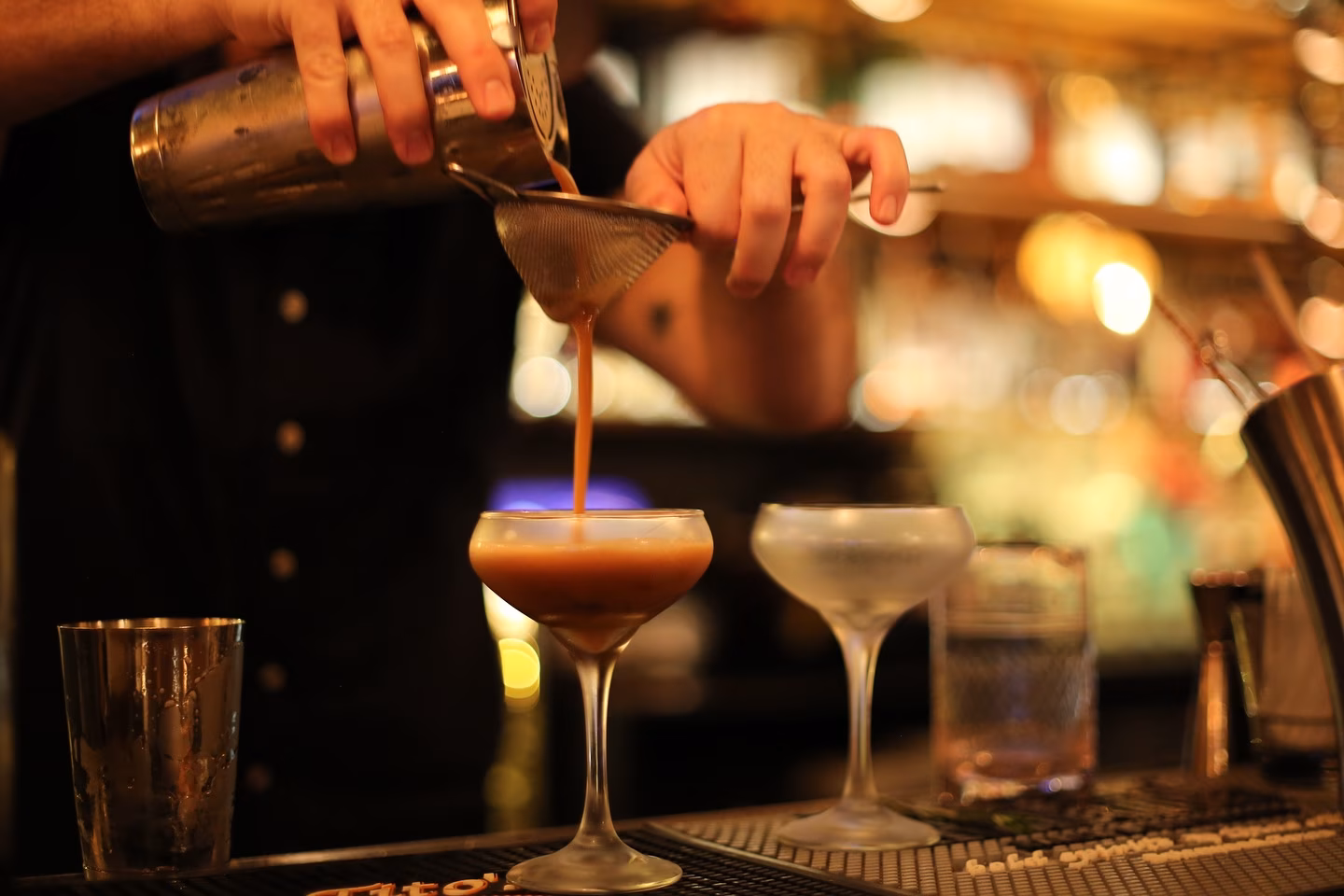 Bartender pouring a cocktail from shaker through strainer into glass.