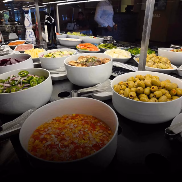 Bowls of fresh vegetables, olives, and salsa on a buffet line.