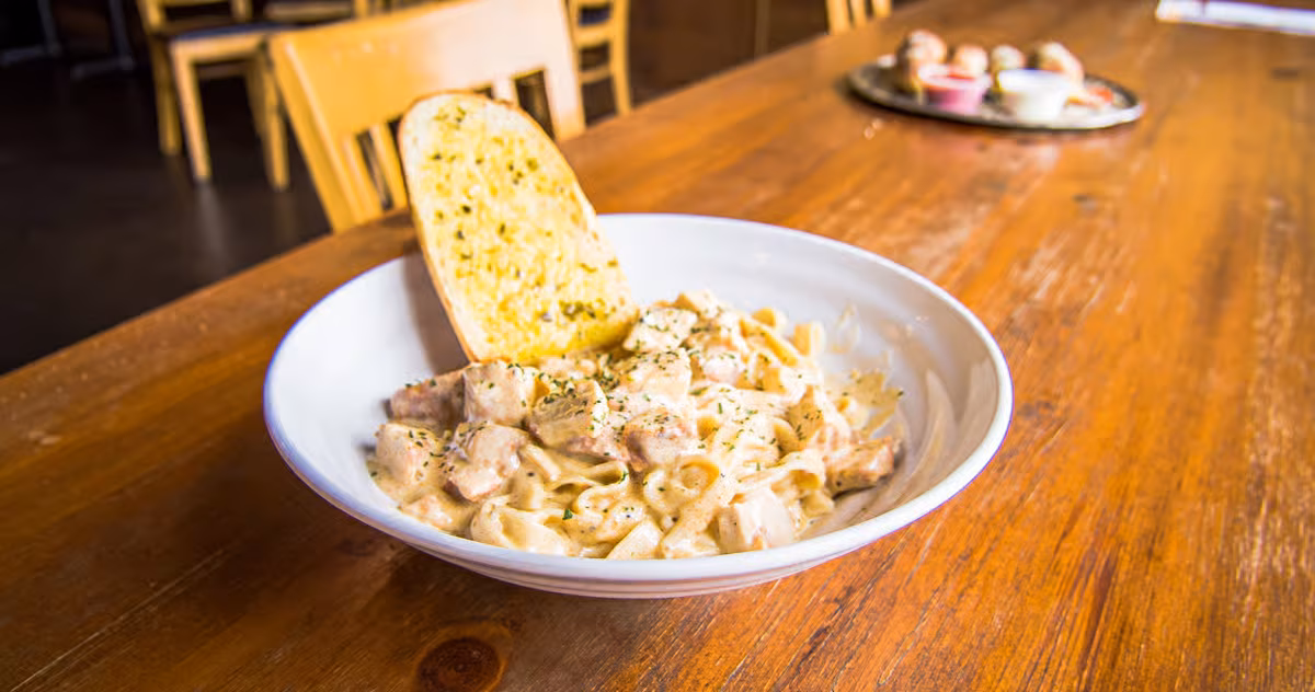 Creamy pasta with chicken, garlic bread, and herbs on wooden table.