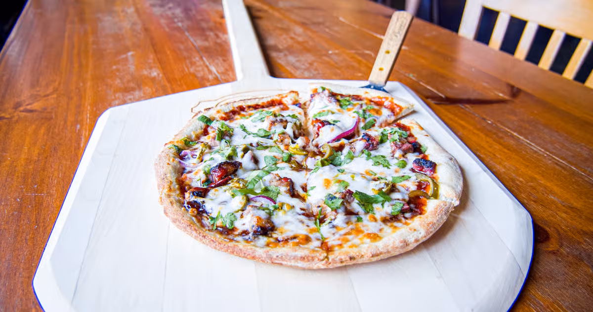 Sliced pizza with melted cheese, green herbs, and onions on a peel.