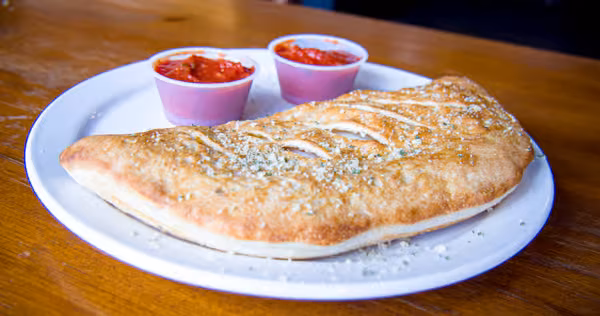 Golden calzone sprinkled with herbs and cheese, with two marinara cups.