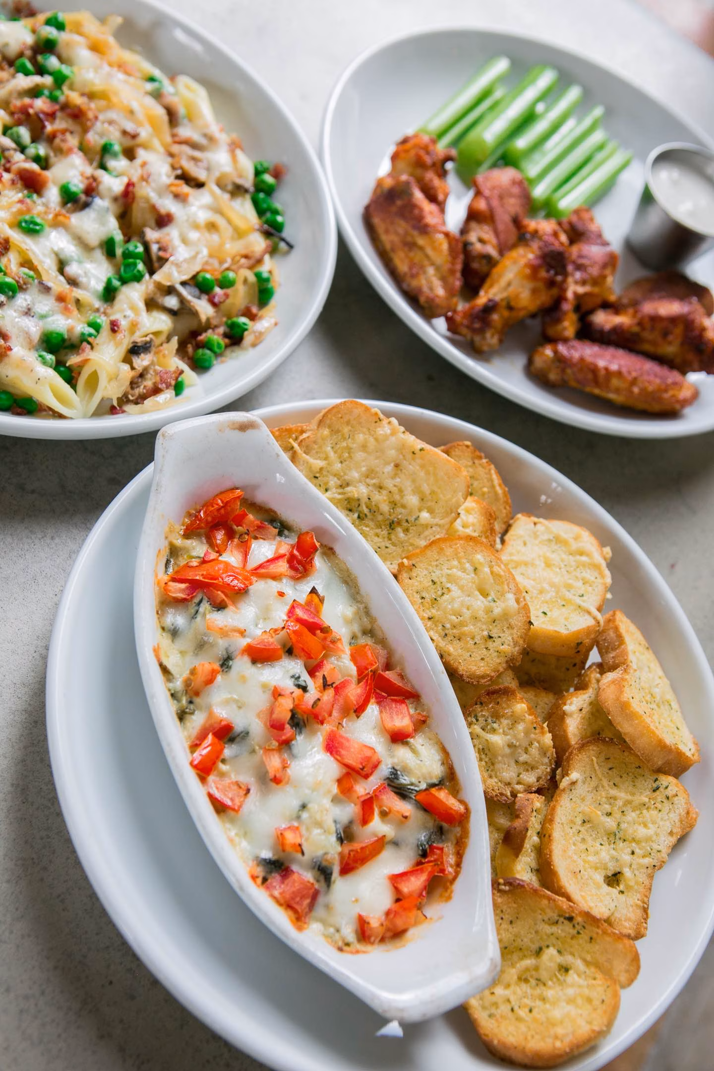 Plates of pasta, chicken wings, cheesy dip, and garlic bread.