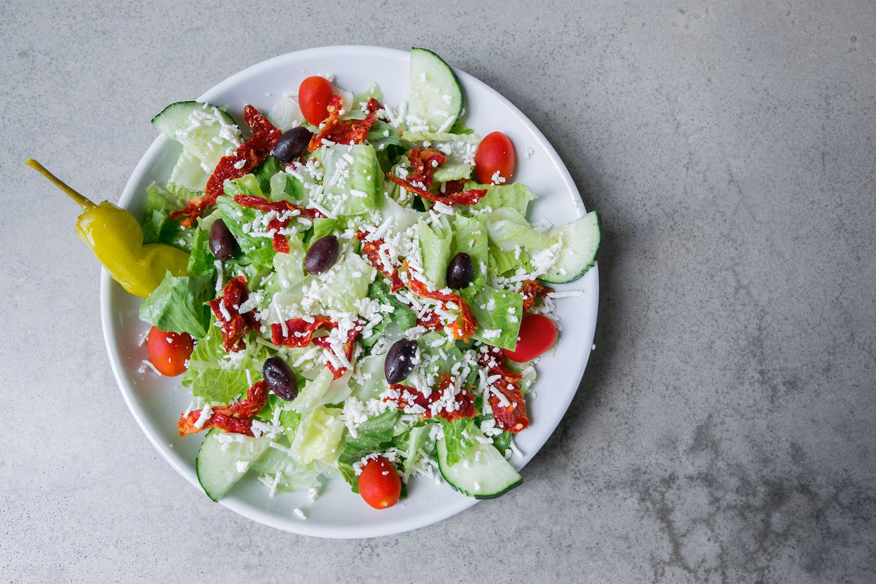 Salad with lettuce, crumbled cheese, olives, tomatoes, cucumber, and pepperoncini.