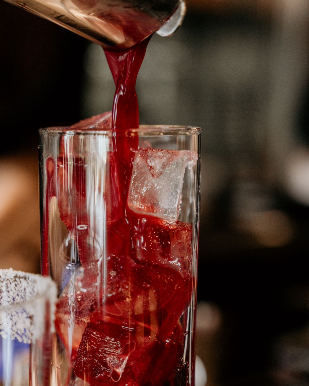 Close-up of red drink pouring into ice-filled glass with salted rim.