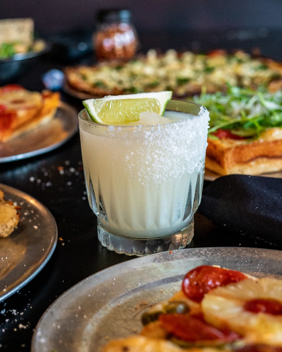Close-up of a salt-rimmed drink with lime, food blurred in background.