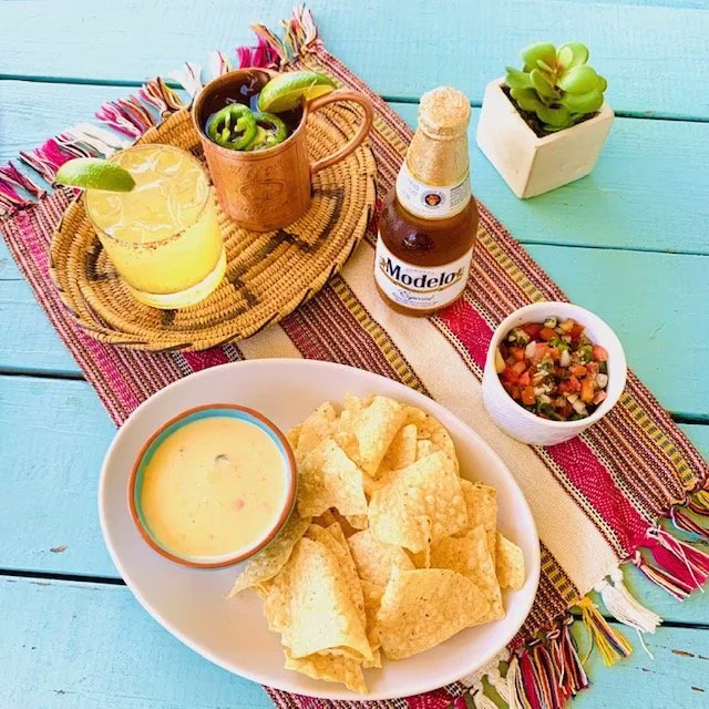 Chips, queso, salsa, beer, and cocktails on a colorful placemat.