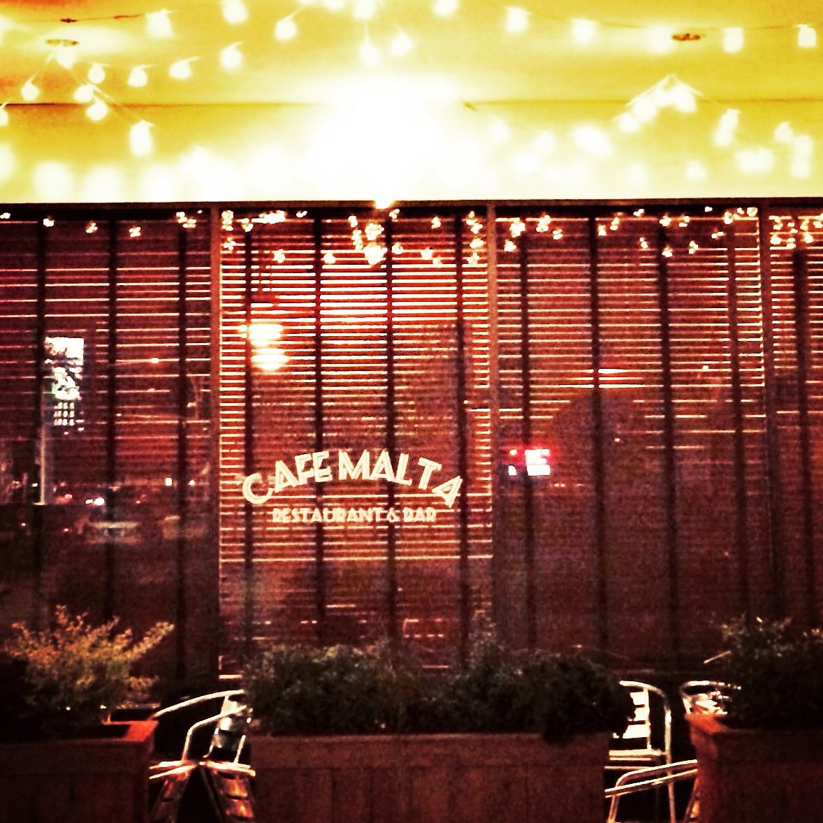 Cafe Malta restaurant exterior at night with string lights and blinds.