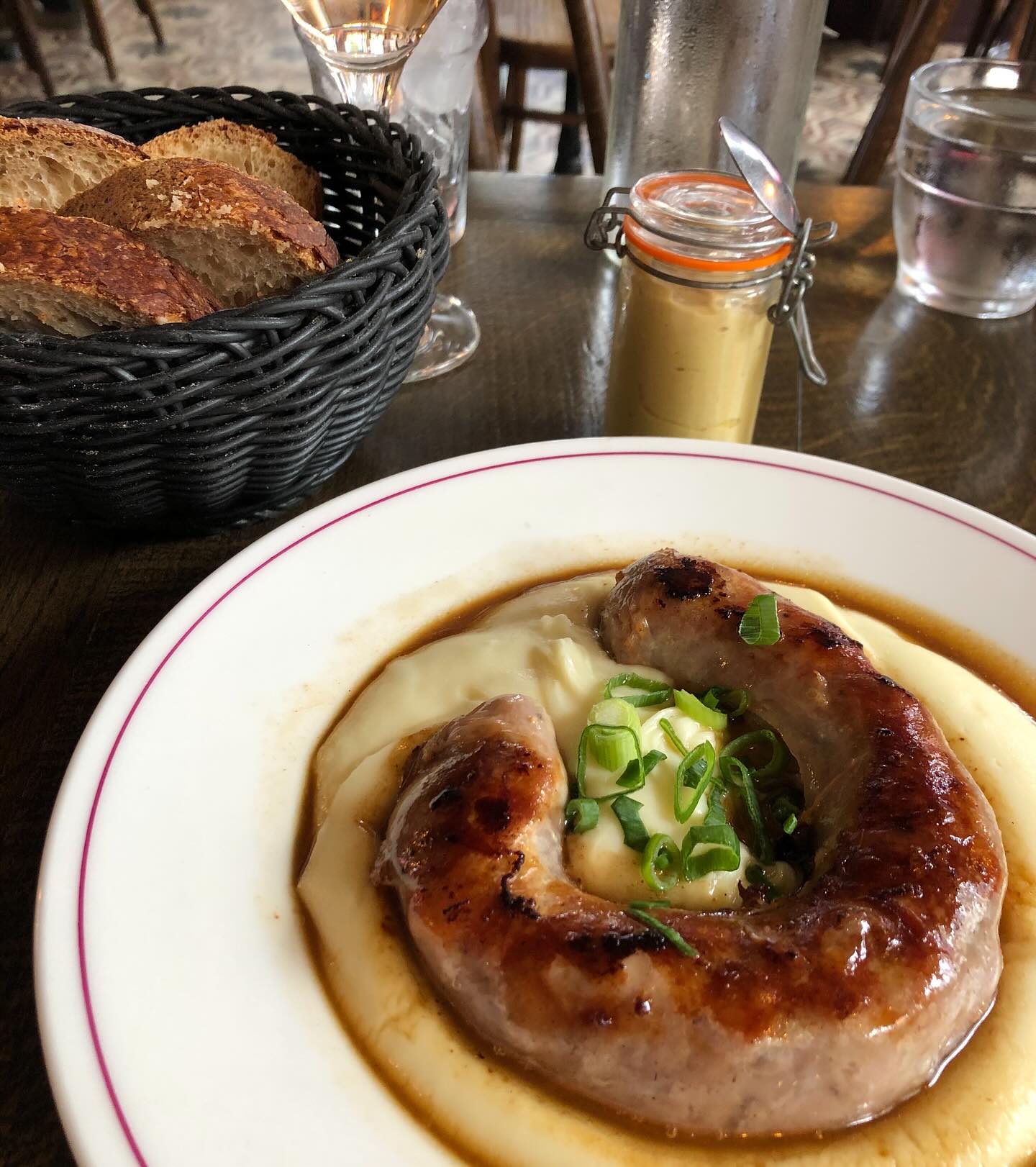Grilled sausage on mashed potatoes with gravy, bread, and mustard.