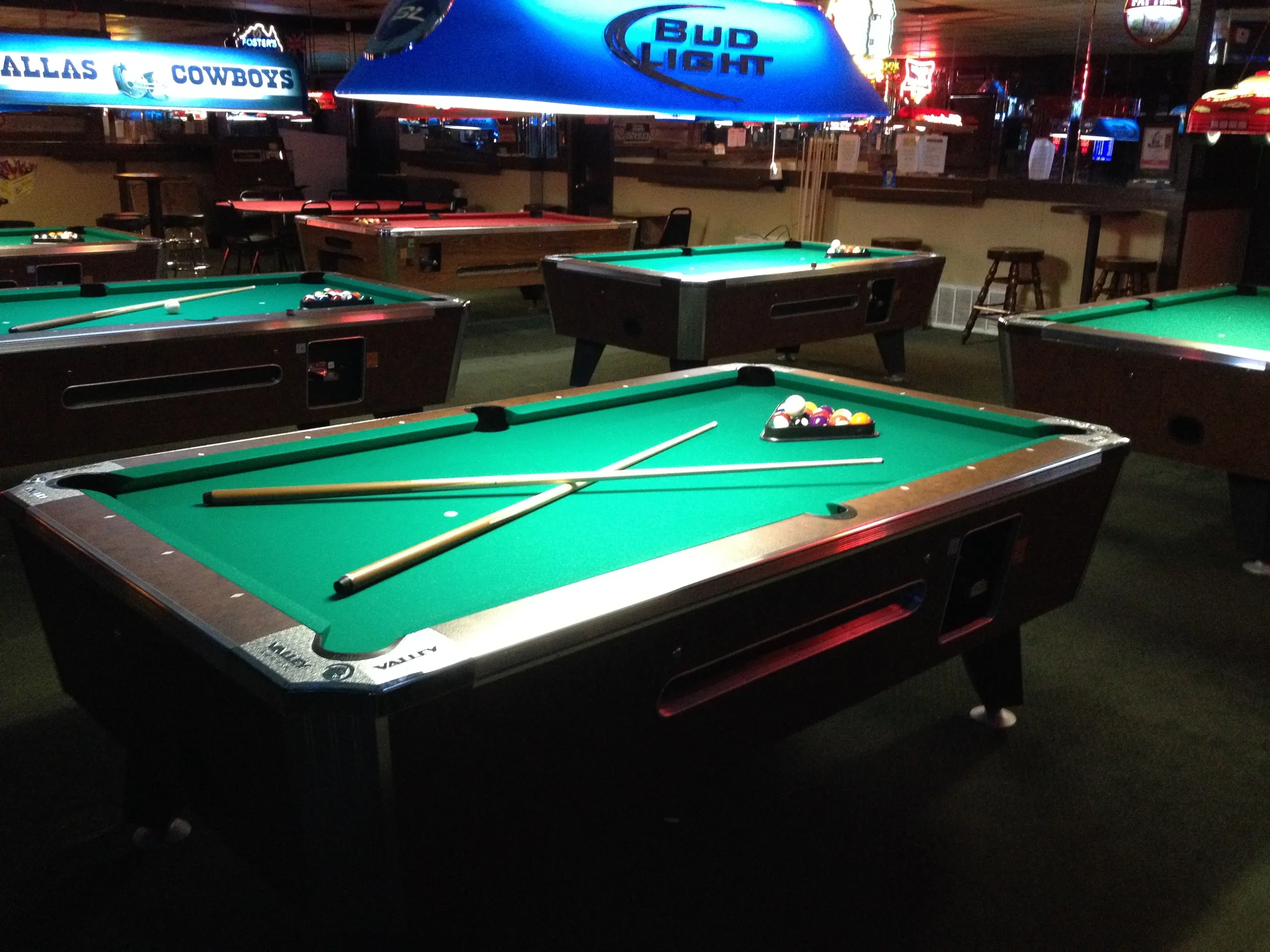 Several pool tables with cues and balls in a dimly lit room.