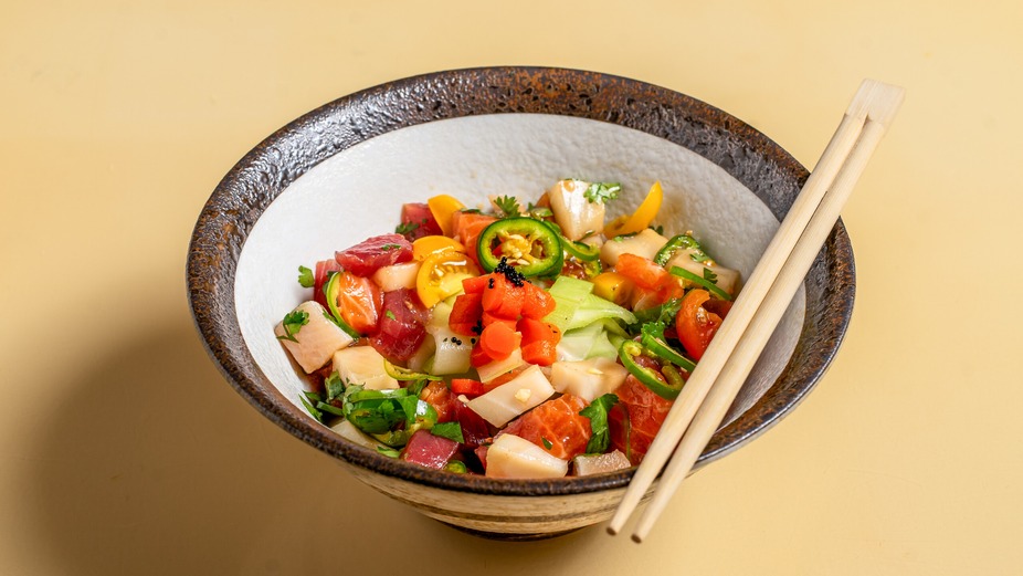 Colorful poke bowl with raw fish, vegetables, jalapeños, and chopsticks.
