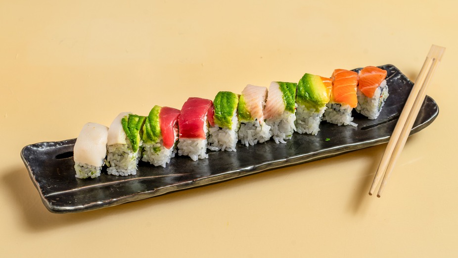 Rainbow sushi rolls on a black plate with chopsticks.