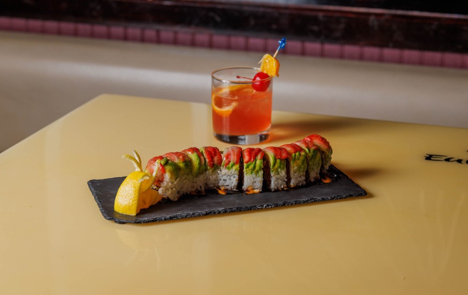 Sushi roll with avocado and red slices, cocktail, on yellow table.