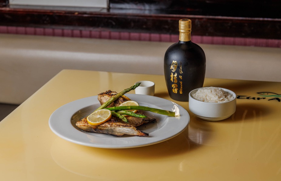 Grilled fish with asparagus, lemon, rice, and a black bottle.