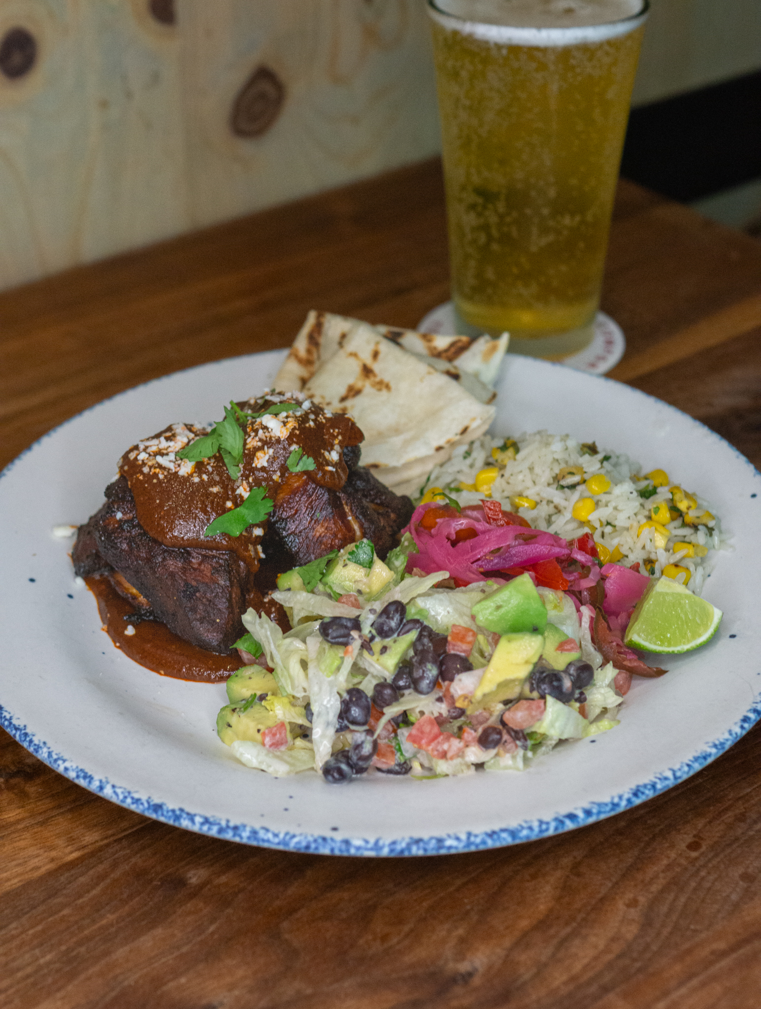 Plate of sauced meat, rice, salad, tortillas, and beer.