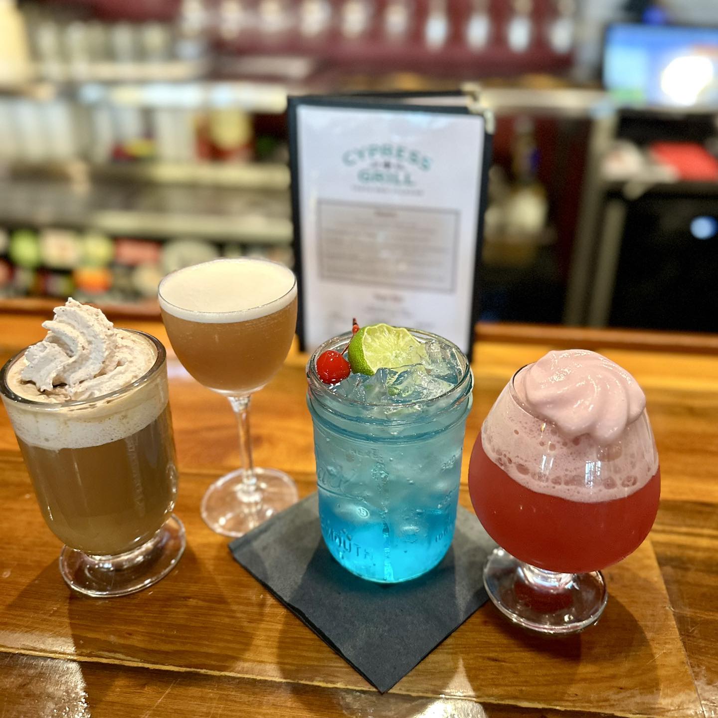 Four different drinks on a wooden bar counter with a menu.