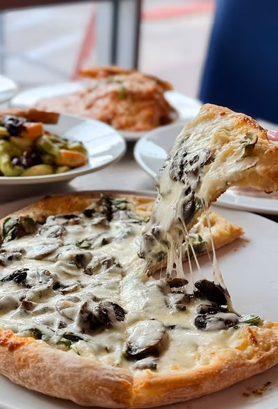 White pizza slice with mushrooms and spinach, lifted with stringy cheese.
