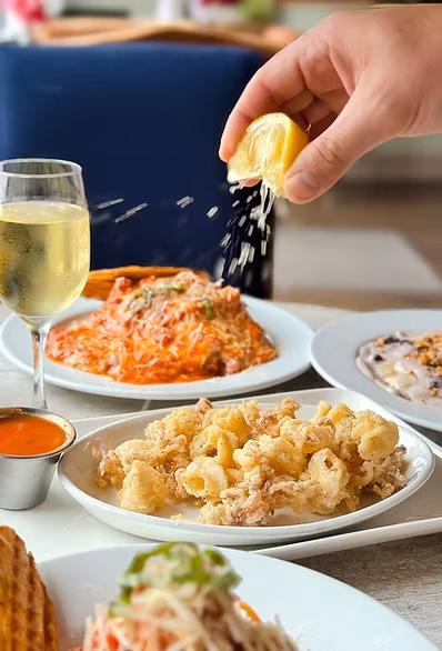 A hand squeezing a lemon over restaurant plates of pasta and calamari.