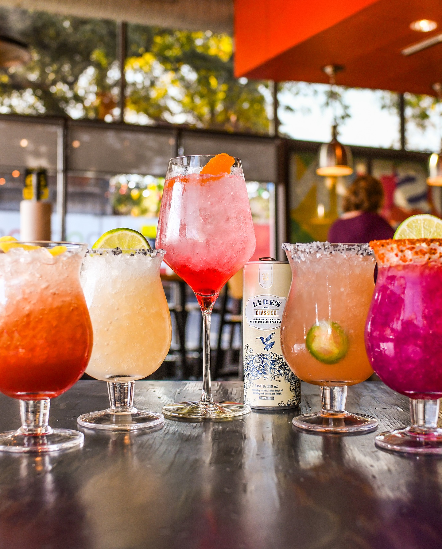 Five colorful drinks and a Lyre's Classico can on a table.