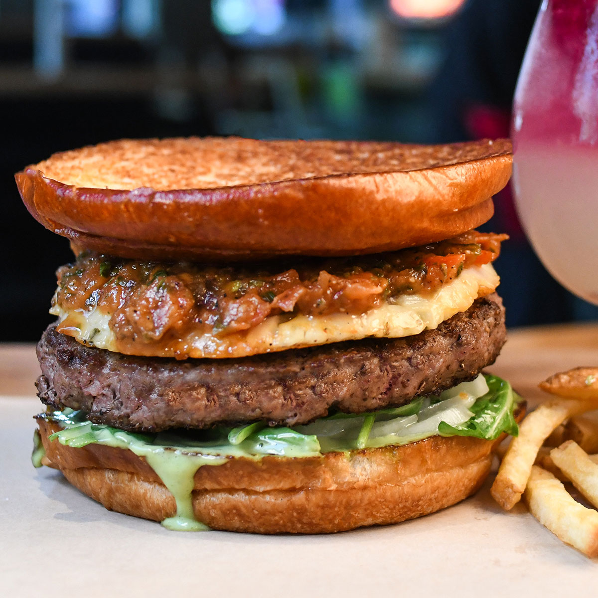 A burger with a thick patty, cheese, salsa, green sauce, and fries.