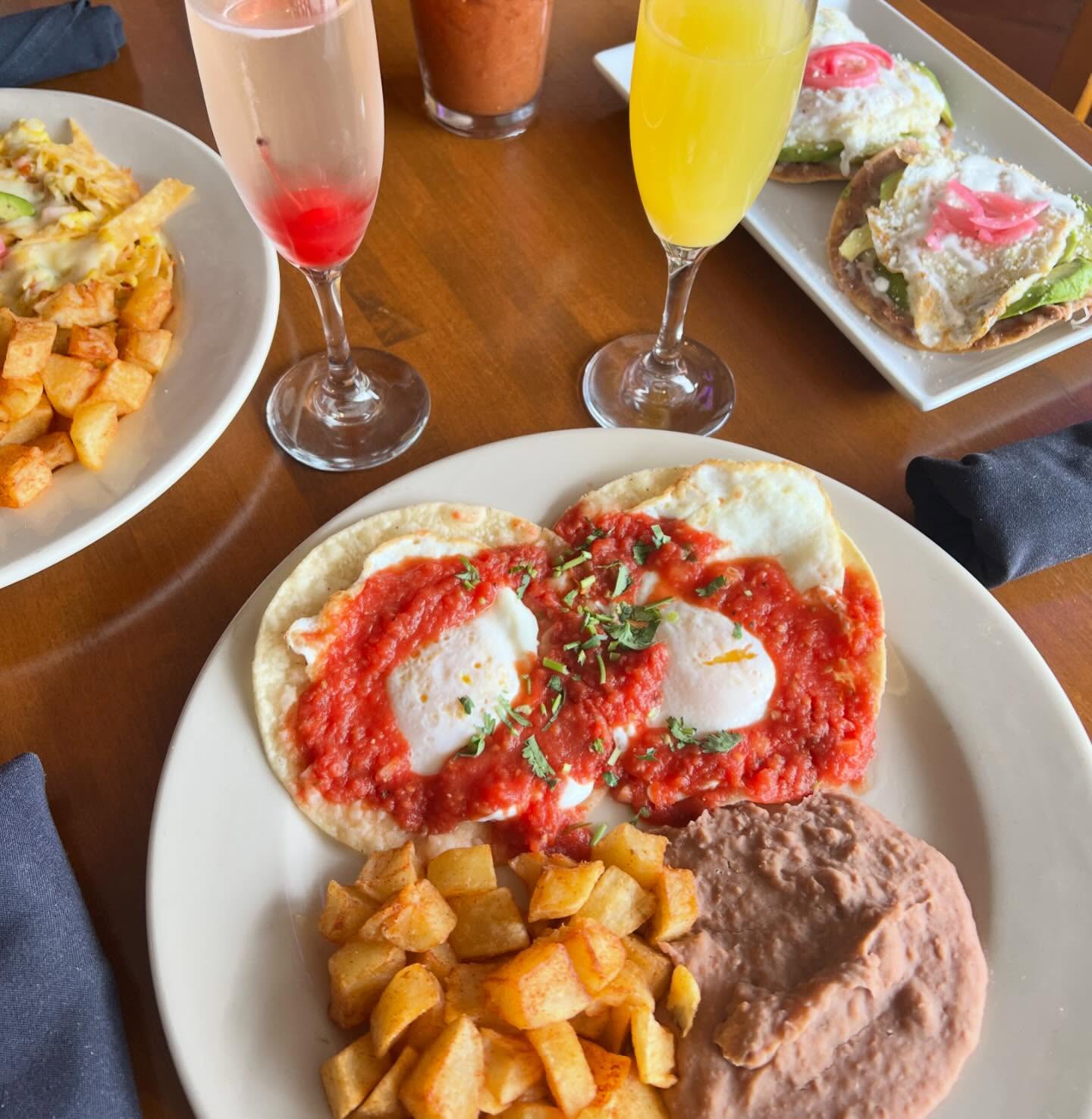 Breakfast spread with huevos rancheros, tostadas, potatoes, and brunch cocktails.