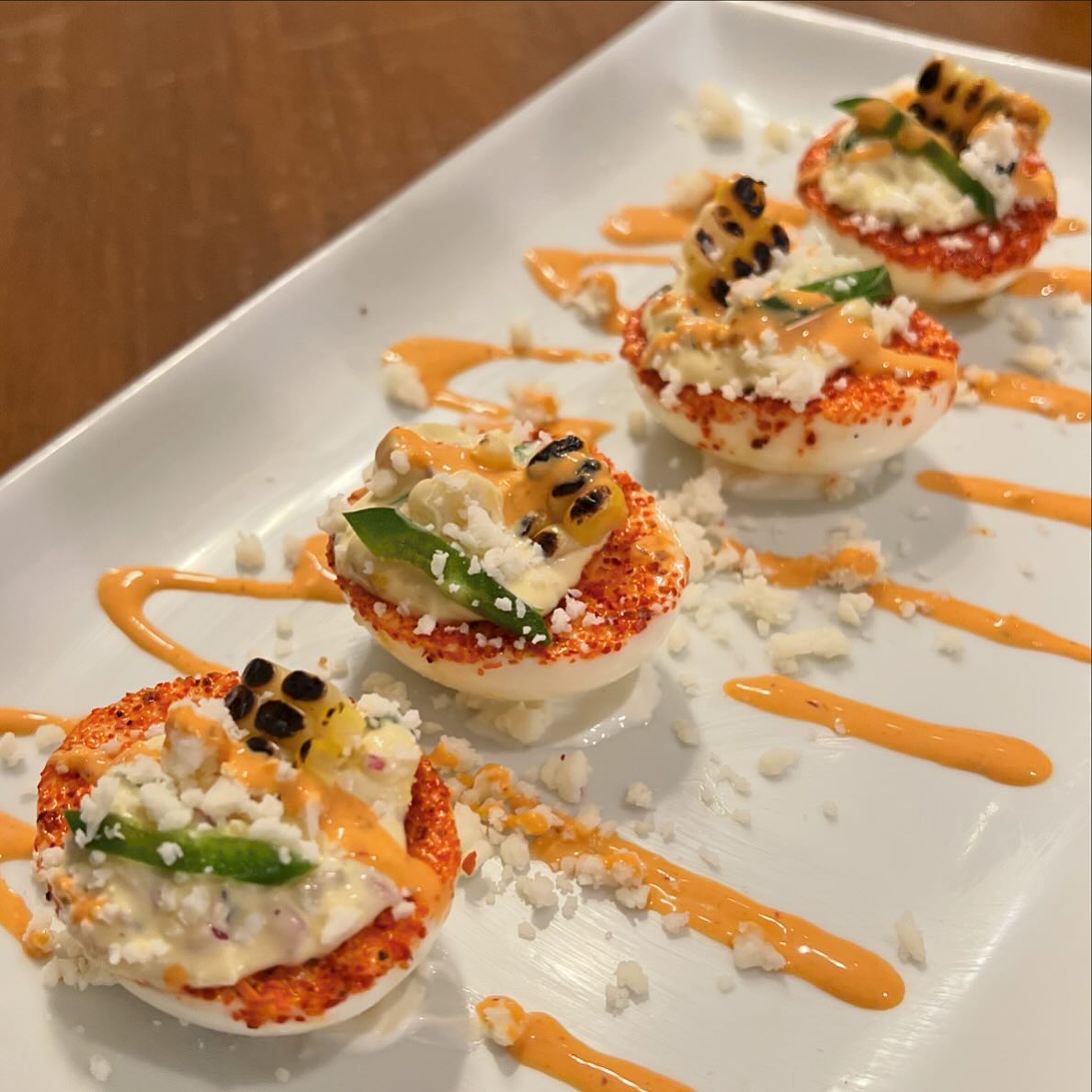 Four deviled eggs with cheese, grilled corn, red spice, and sauce.