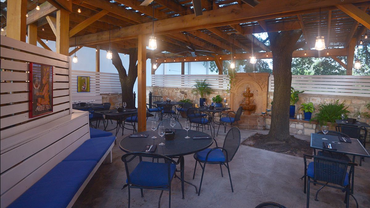 Outdoor restaurant patio with tables, chairs, trees, and fountain.