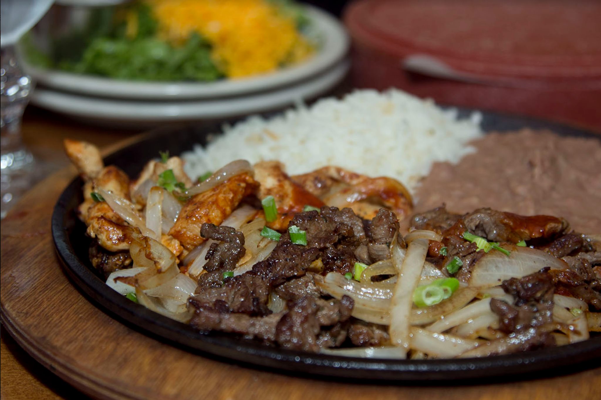 Sizzling platter with chicken, beef, onions, rice, and refried beans.