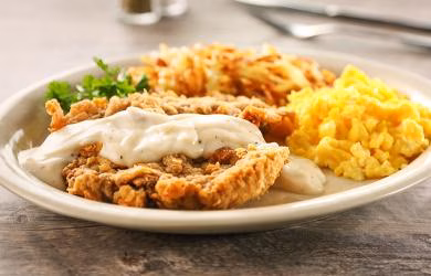 Country fried steak with gravy, hash browns, and scrambled eggs.