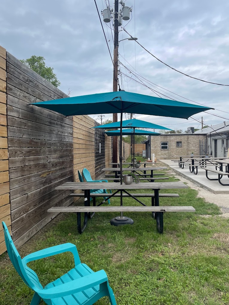 Outdoor seating area with picnic tables, teal umbrellas, and chairs on grass.