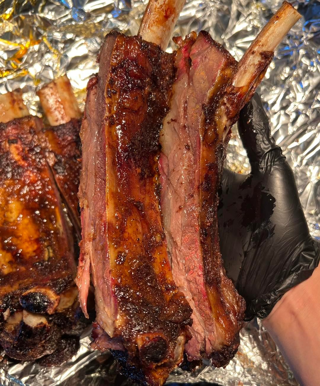 Gloved hand holds smoked beef ribs with a reddish smoke ring.
