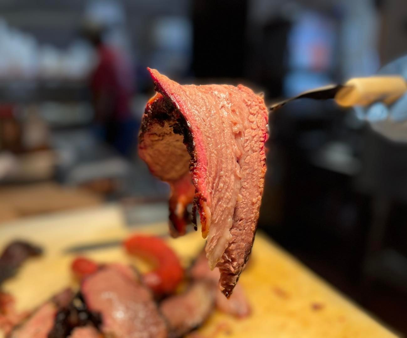 Thick slice of smoked meat with pink smoke ring on fork.