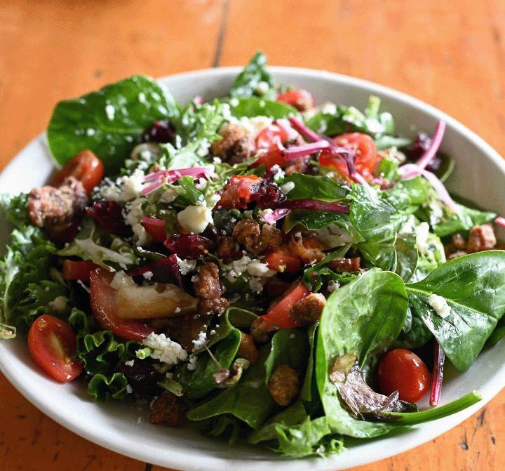 Mixed green salad with cherry tomatoes, crumbled cheese, and crunchy pieces.