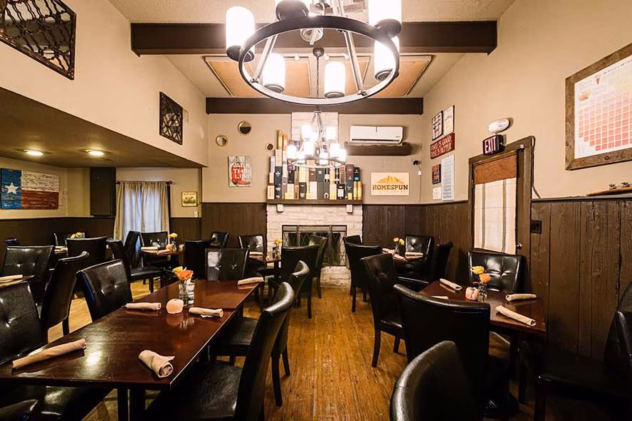 Rustic restaurant interior with dark tables, leather chairs, and fireplace.
