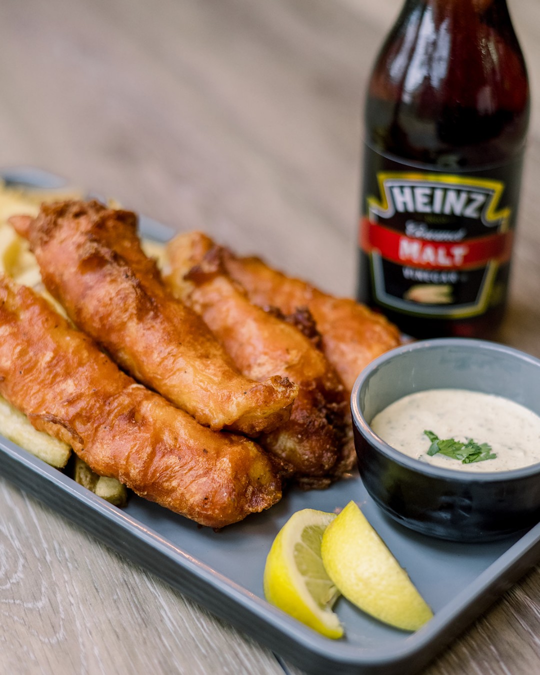 Fried fish and chips with sauce, lemon, and Heinz malt vinegar bottle.