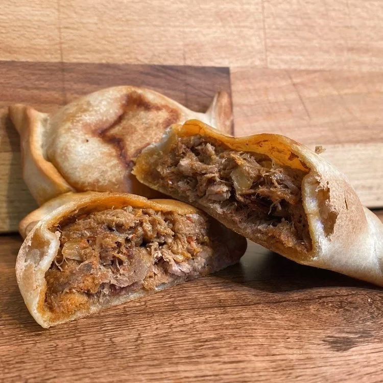 Three golden empanadas on wood, two split revealing meat filling.