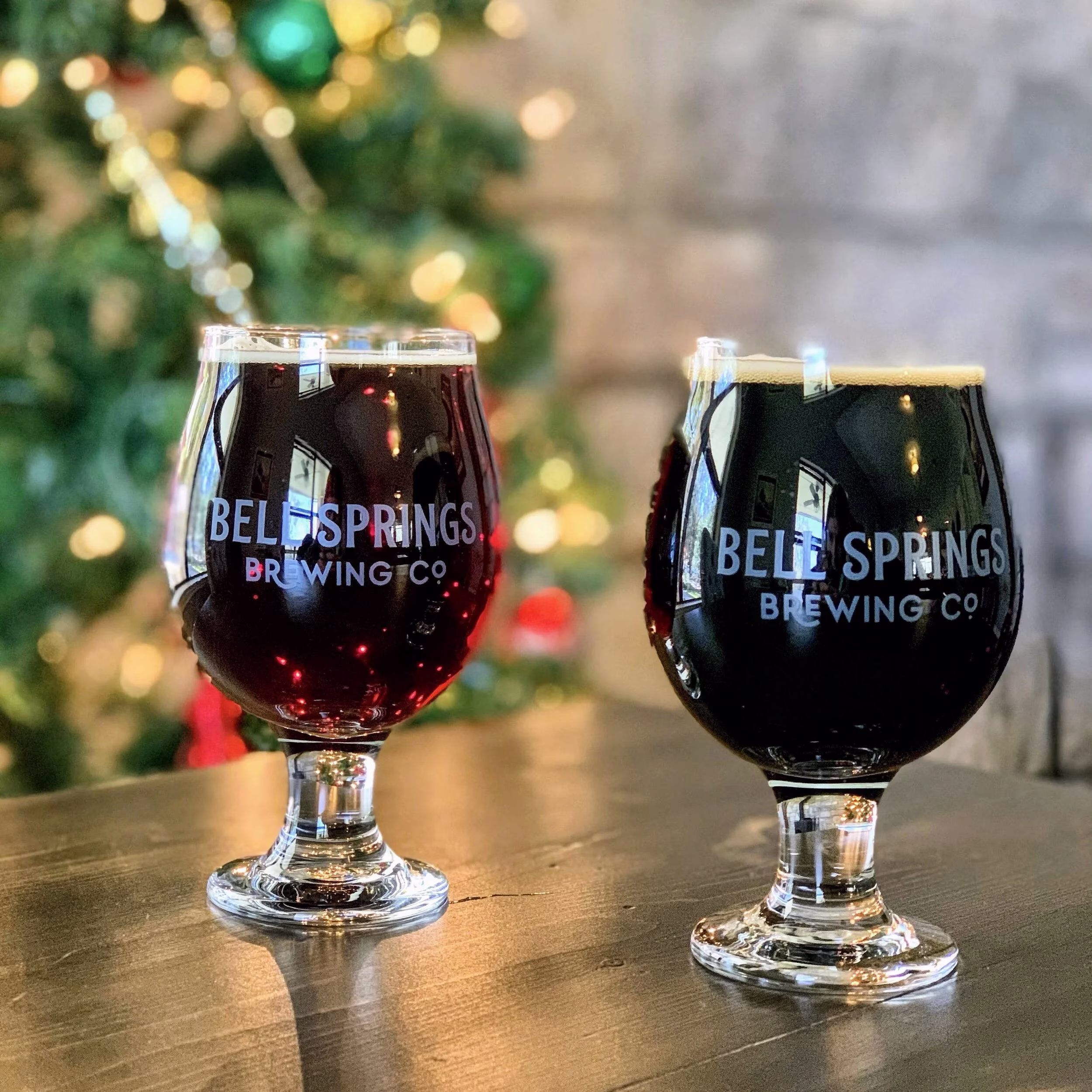 Two dark beers from Belle Springs Brewing Co. near a Christmas tree.