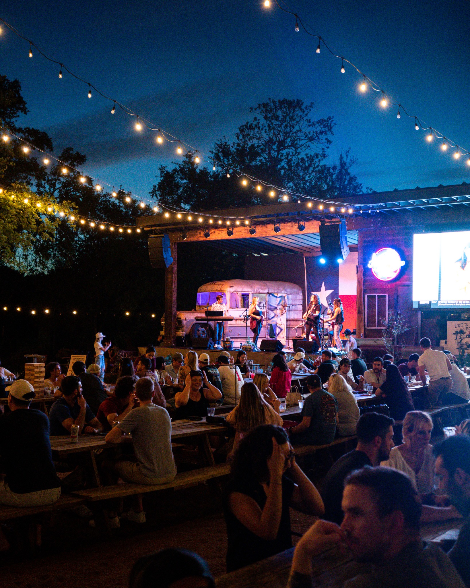 People enjoy an outdoor concert at night with string lights.