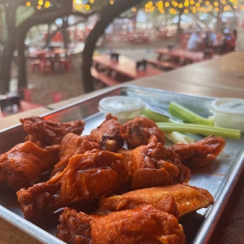 Tray of red chicken wings, celery, and dip, outside a restaurant.