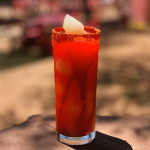 Tall glass with red drink, chili-salted rim, and white garnish.