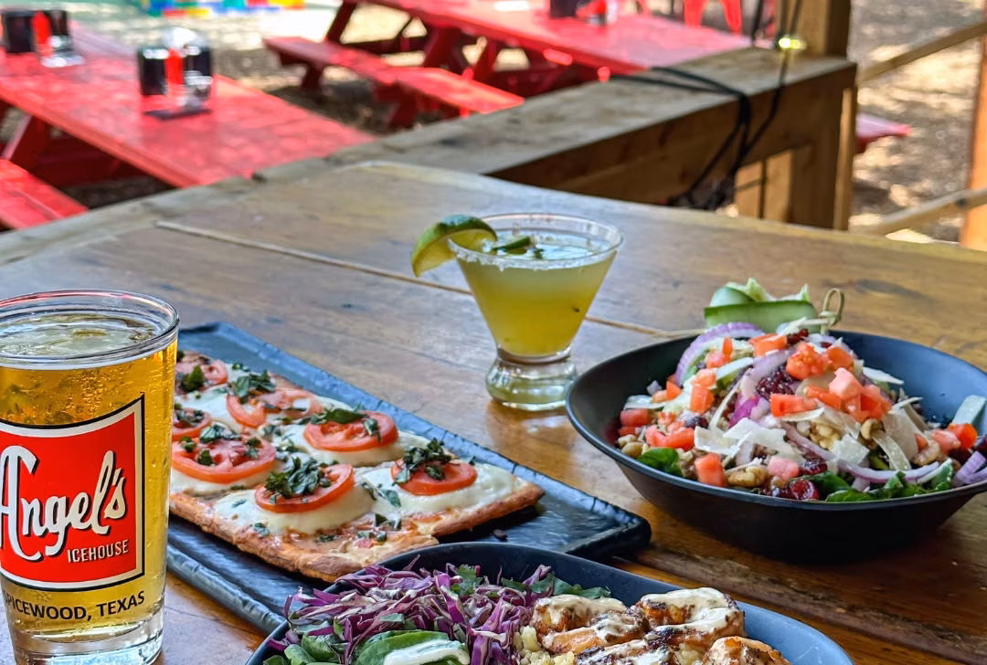 Beer, flatbread, salad, and margarita on an outdoor table.