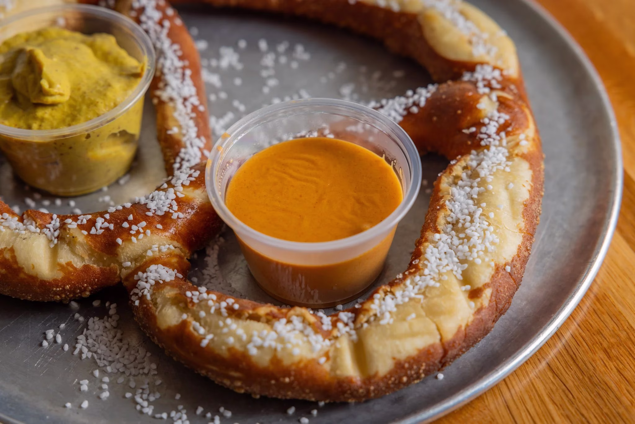 One salted pretzel with yellow mustard and orange dipping sauce.
