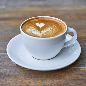 White cup of coffee with heart latte art on a wooden surface.