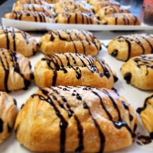 Freshly baked pastries with dark chocolate drizzle arranged in rows.