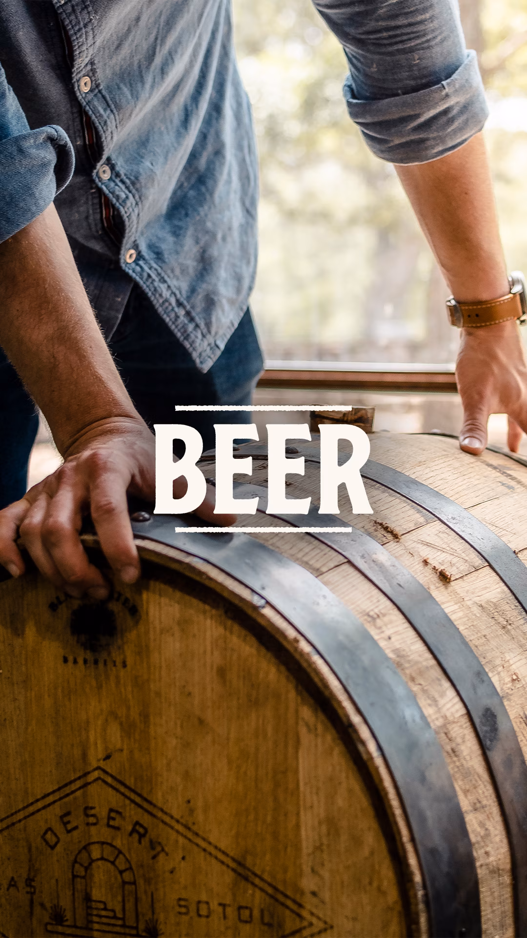 Man in denim shirt, hands on wooden barrel with 'BEER' text.